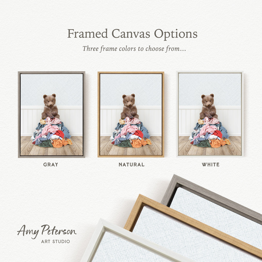 The image is a framed canvas option showcasing three different frame colors: gray, natural, and white. The canvas features a teddy bear sitting on a pile of clothes.