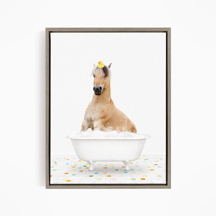 A light brown horse is sitting in a white bathtub filled with bubbles, with a yellow rubber duck perched on its head.