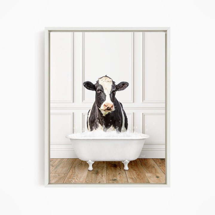 A black and white cow is standing in a white bathtub filled with water, creating a humorous and whimsical scene.
