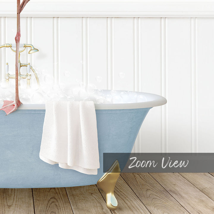 A blue claw-foot bathtub filled with bubbles, with a white towel hanging on the side and a gold claw-foot bathtub leg visible.