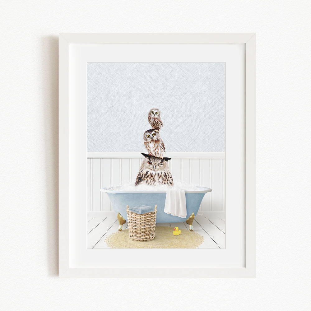 A framed image depicting a bird perched on a bathtub filled with bubbles, surrounded by a yellow rubber duck and a woven basket.
