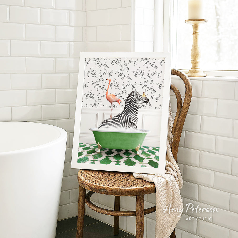 A framed print of a zebra sitting in a green bathtub, with a pink flamingo perched on the zebra's back, is displayed on a wooden chair in a bathroom setting.