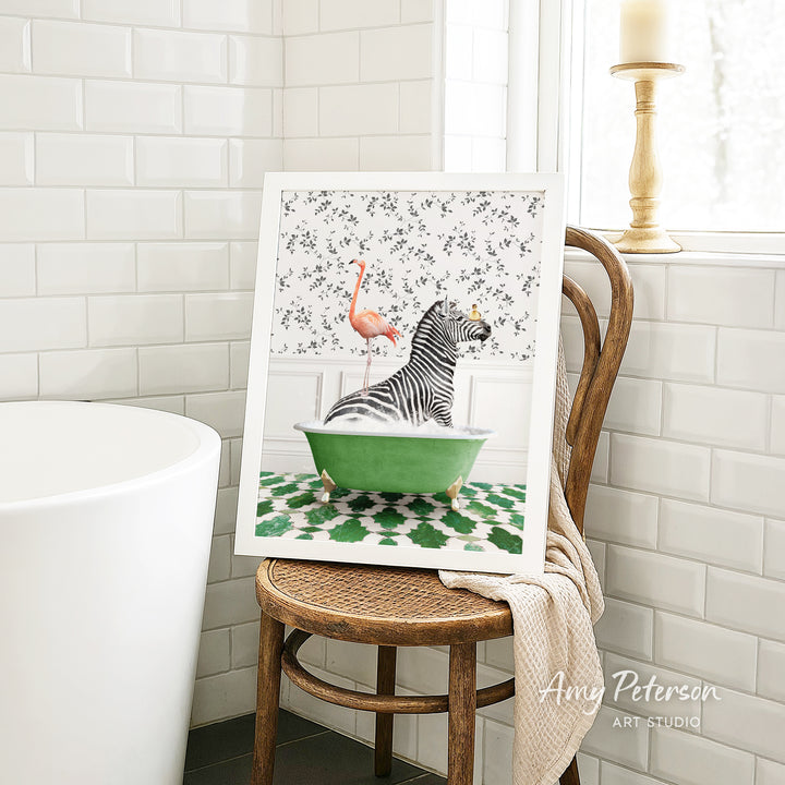 A framed print of a zebra sitting in a green bathtub, with a pink flamingo perched on the zebra's back, is displayed on a wooden chair in a bathroom setting.