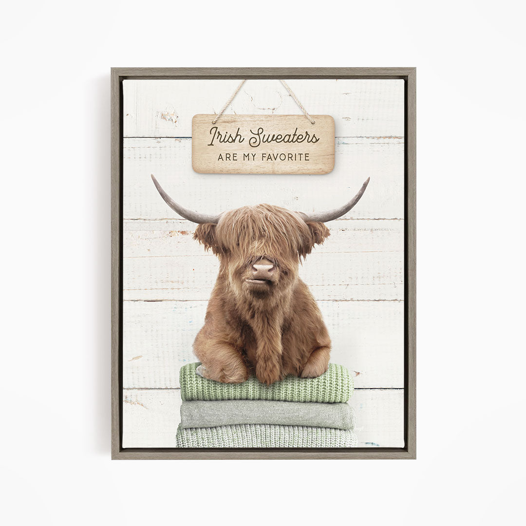 A framed image of a Highland cow sitting on a stack of green blankets, with a sign above that says "Irish Sweaters are my favorite".