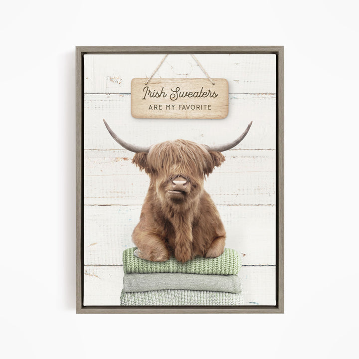 A framed image of a Highland cow sitting on a stack of green blankets, with a sign above that says "Irish Sweaters are my favorite".