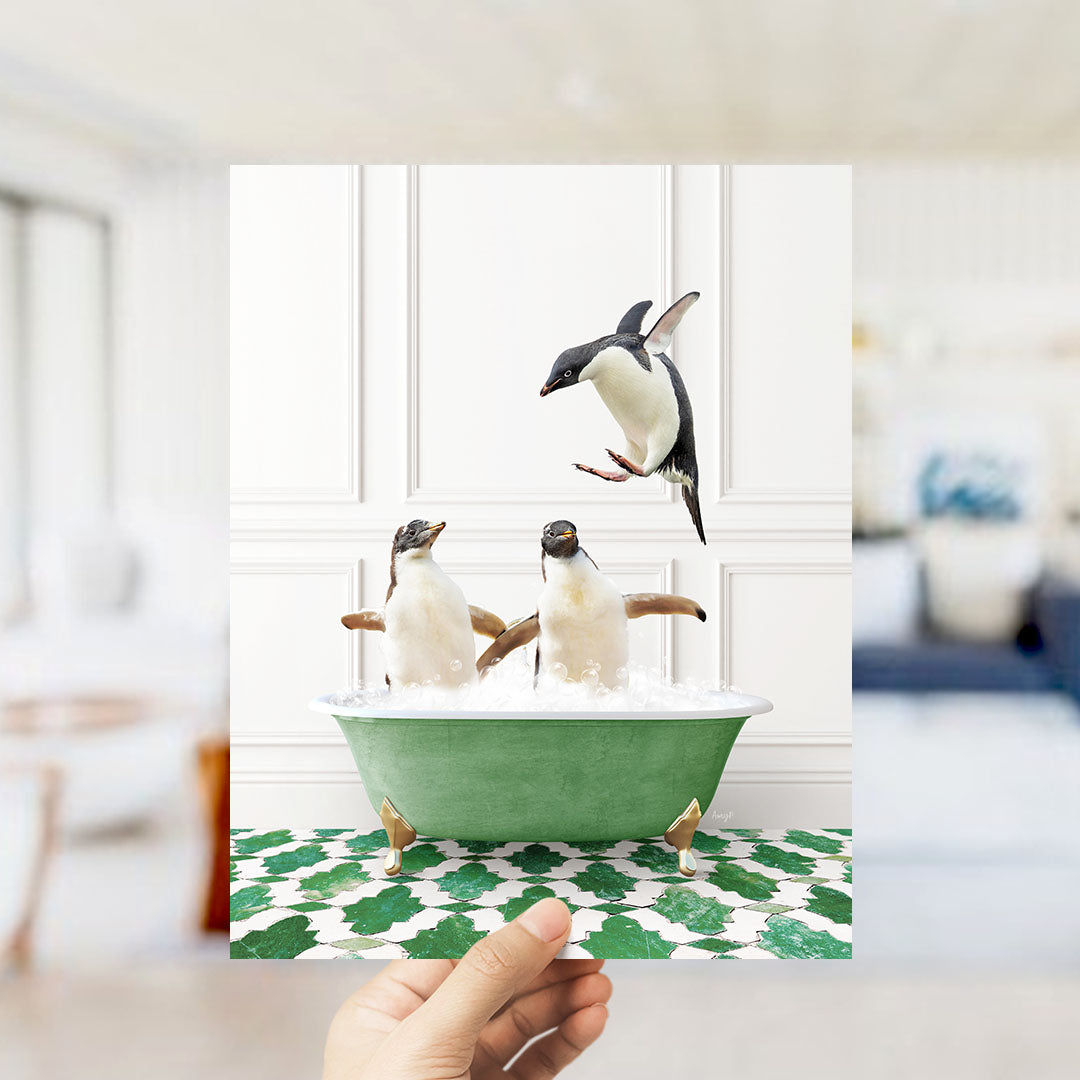 A hand holds up a framed image of two penguins sitting in a green bathtub, with one penguin flying towards the other.