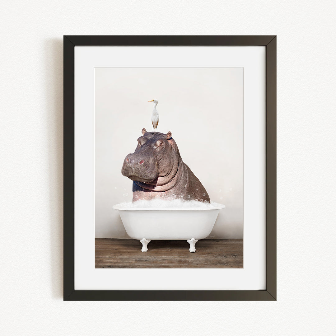 A framed image depicting a large hippopotamus sitting in a bathtub, with a seagull perched on its head.