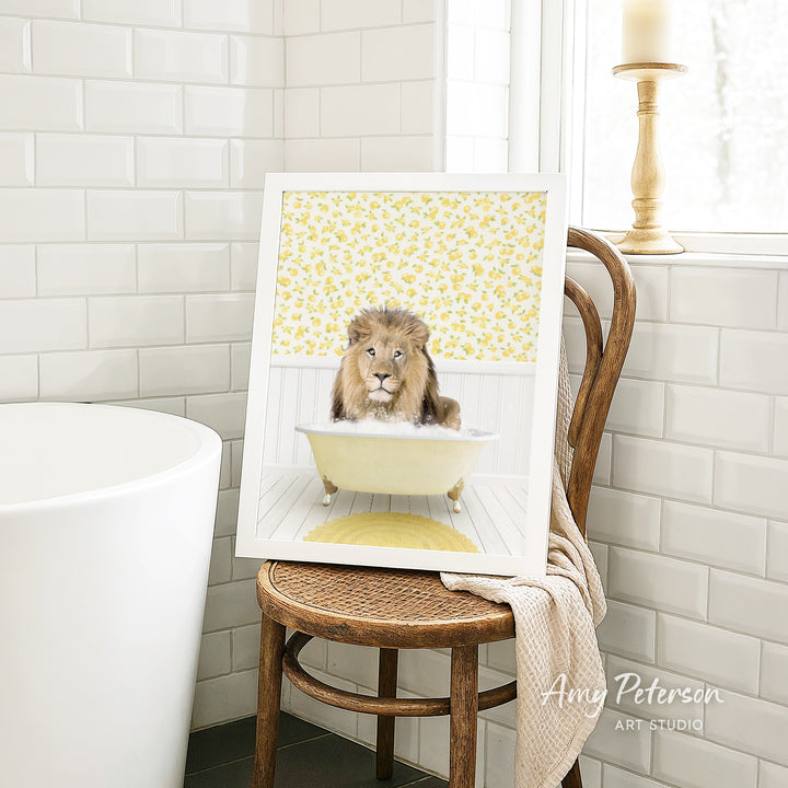 A framed image of a lion sitting in a bathtub, surrounded by yellow flowers, is displayed on a wooden chair in a bathroom setting.