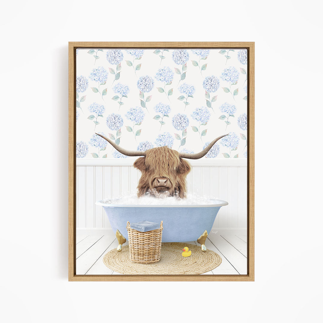 A brown cow with long horns is sitting in a blue bathtub filled with water, surrounded by a wicker basket and rubber duckies.