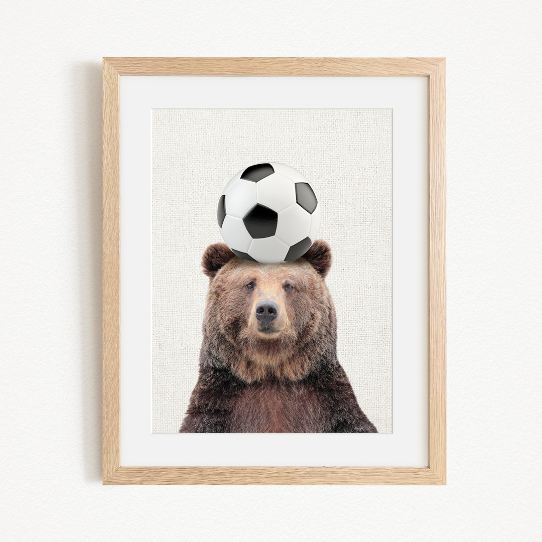 A brown bear balancing a soccer ball on its head.