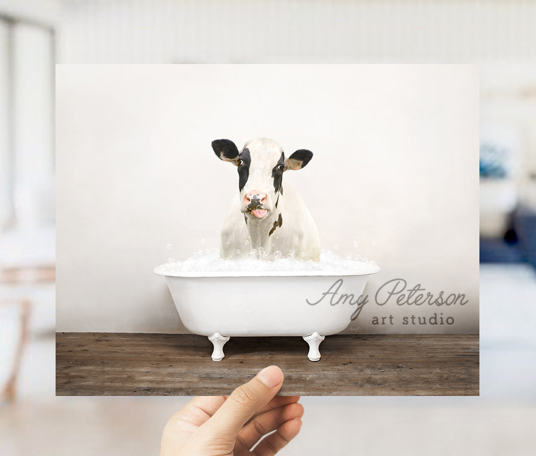 a person holding up a picture of a cow in a bathtub