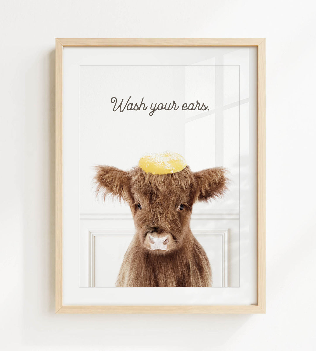 A framed image of a brown cow with a yellow object on its head, accompanied by the text "Wash your ears."
