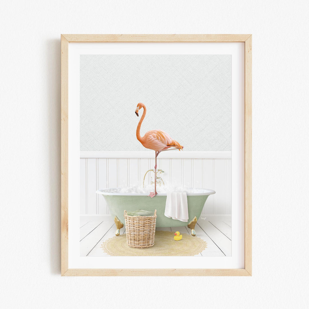 A framed image depicting a pink flamingo standing on a green bathtub, with a basket of bath toys and a towel nearby.