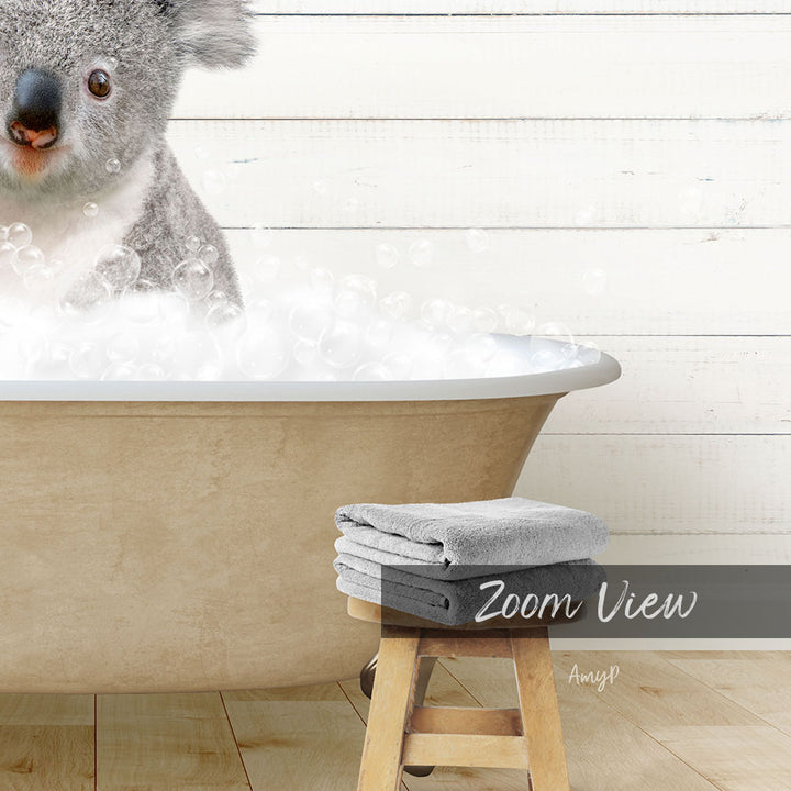 A koala is sitting in a bathtub filled with bubbles, with a towel and stool visible in the foreground.