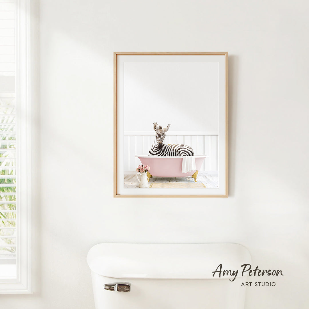 A framed image of a zebra sitting in a pink bathtub, with a window and a white toilet visible in the background.