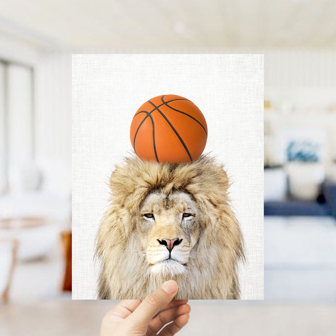 A hand holds up a framed image of a lion with a basketball on its head.