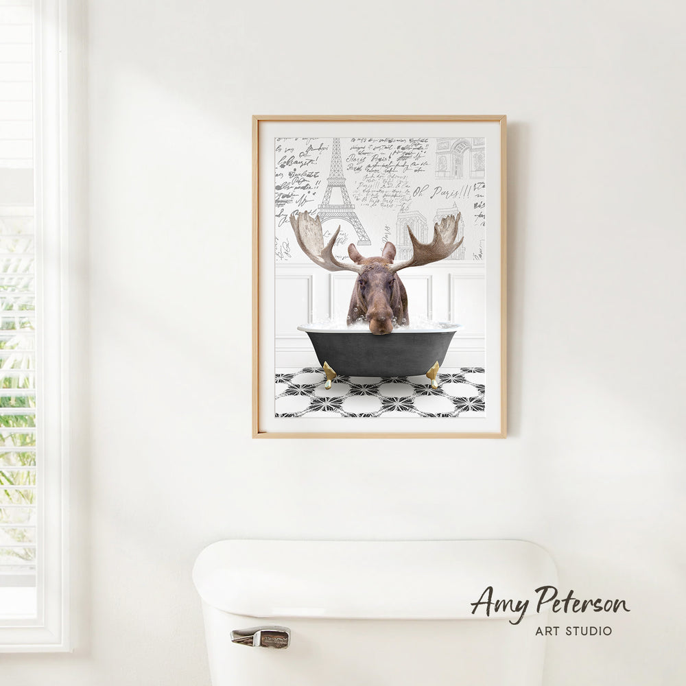 A framed image of a moose sitting in a bathtub, with a black and white checkered floor and a window in the background.