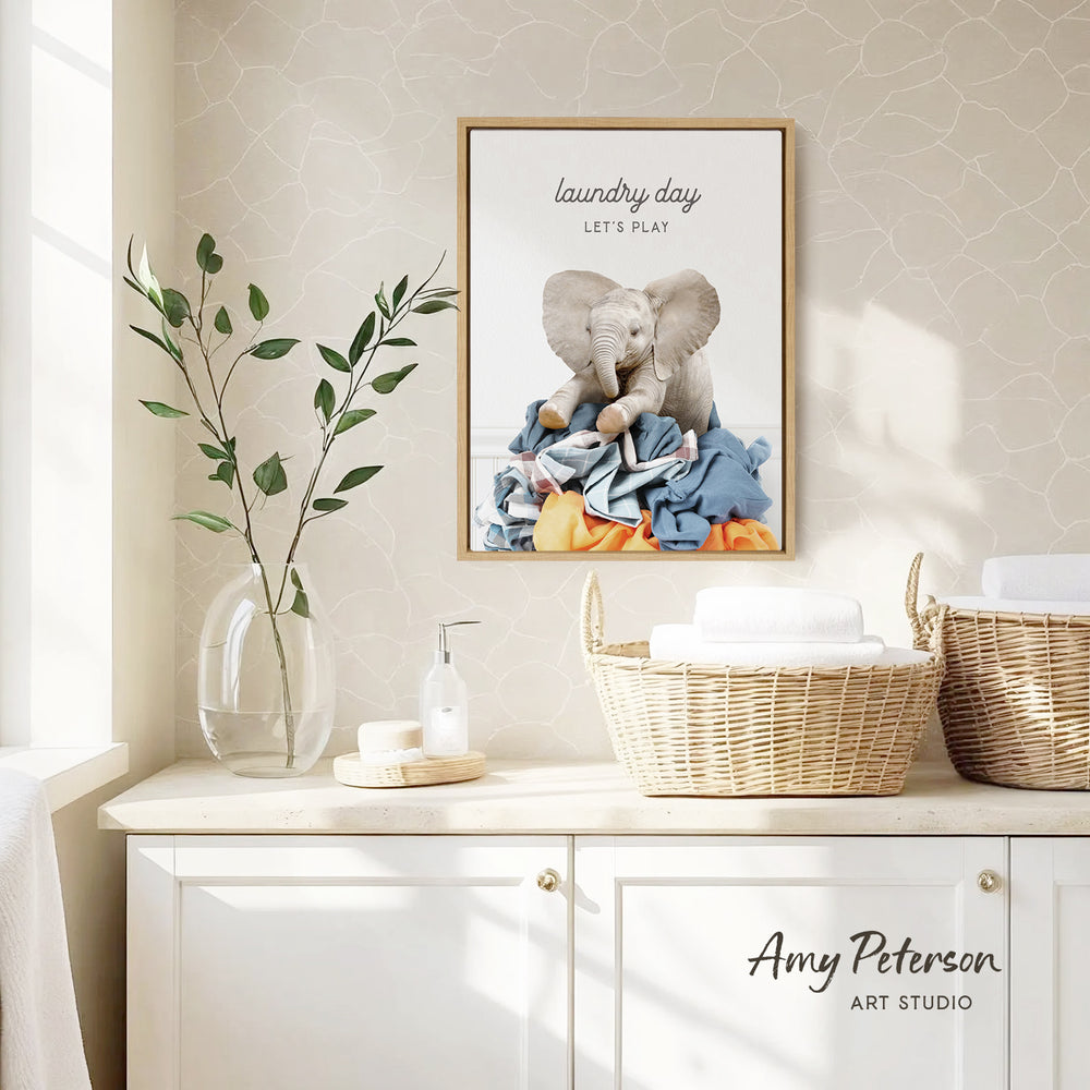 a framed poster of an elephant sitting on laundry, hanging on a wall above a white cabinet with baskets.
