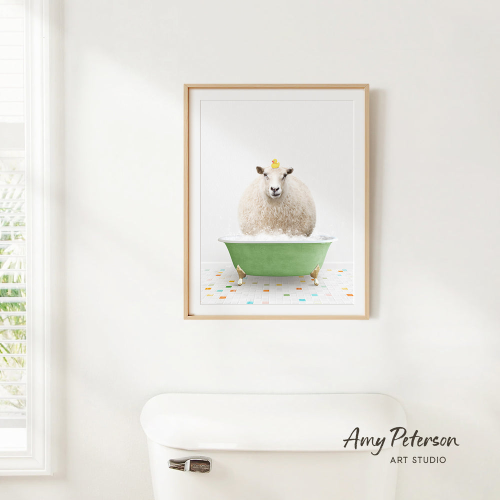 A framed image of a sheep sitting in a green bathtub, with a yellow object on its head, is hanging on a white wall.